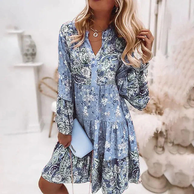 Vrouw in blauwe bloemenjurk met lange mouwen, houdt een lichtblauwe clutch vast. Modieuze dameskleding, casual lente- en zomeroutfit.