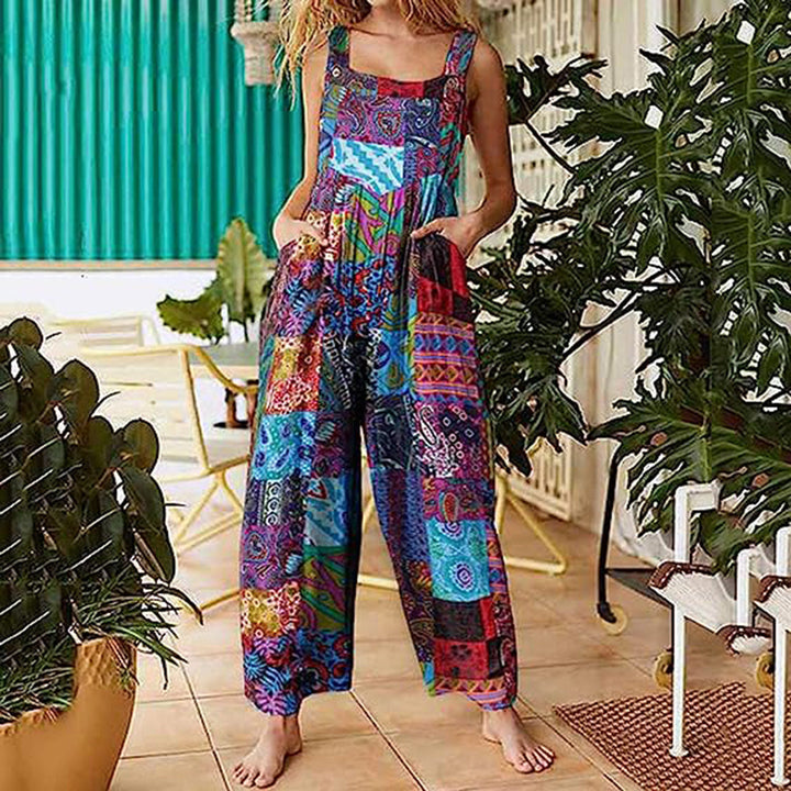 Vrouw in kleurrijke patchwork jumpsuit met etnisch patroon, staand op terras met planten. Trendy damesmode, bohemian stijl, zomeroutfit.