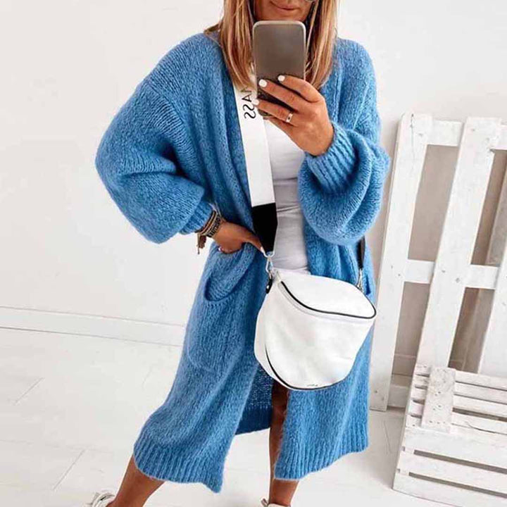 Vrouw in blauwe gebreide cardigan met lange mouwen, witte tas en smartphone, casual mode, trendy herfstkleding, comfortabele damesoutfit.