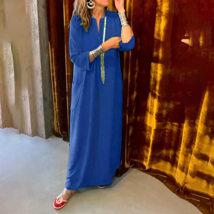 Vrouw in blauwe kaftan met zilveren armbanden, staand voor een goudbruine gordijn. Mode, traditionele kleding, elegante stijl.
