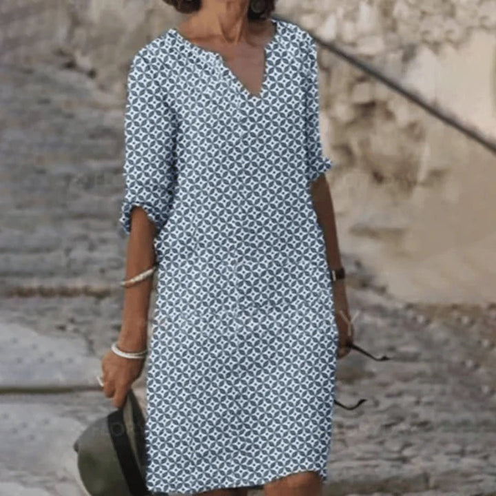 Vrouw in blauwe zomerjurk met geometrisch patroon, wandelend op een stenen pad. Perfect voor casual lente- en zomermode.