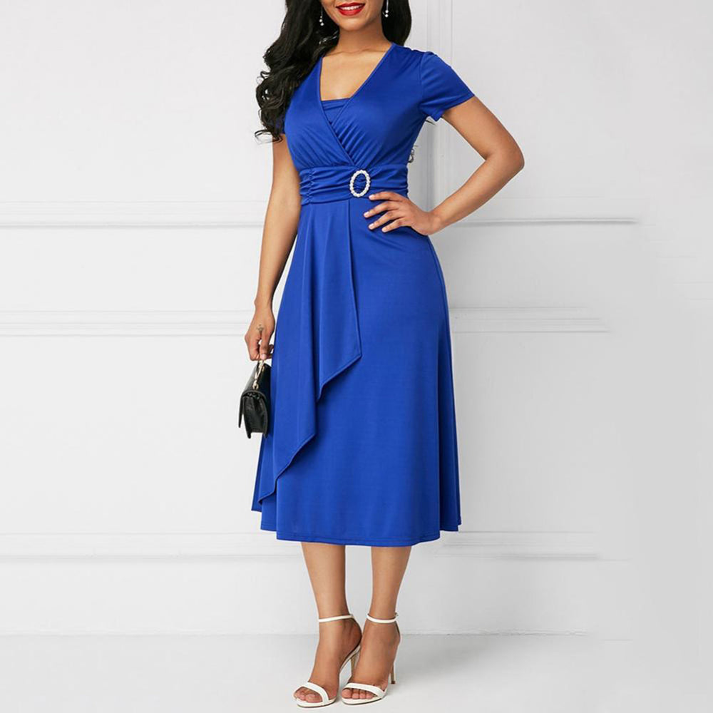 Vrouw in elegante blauwe jurk met V-hals en riemdetail, draagt witte sandalen en zwarte handtas. Perfecte outfit voor avondfeest of cocktailparty.