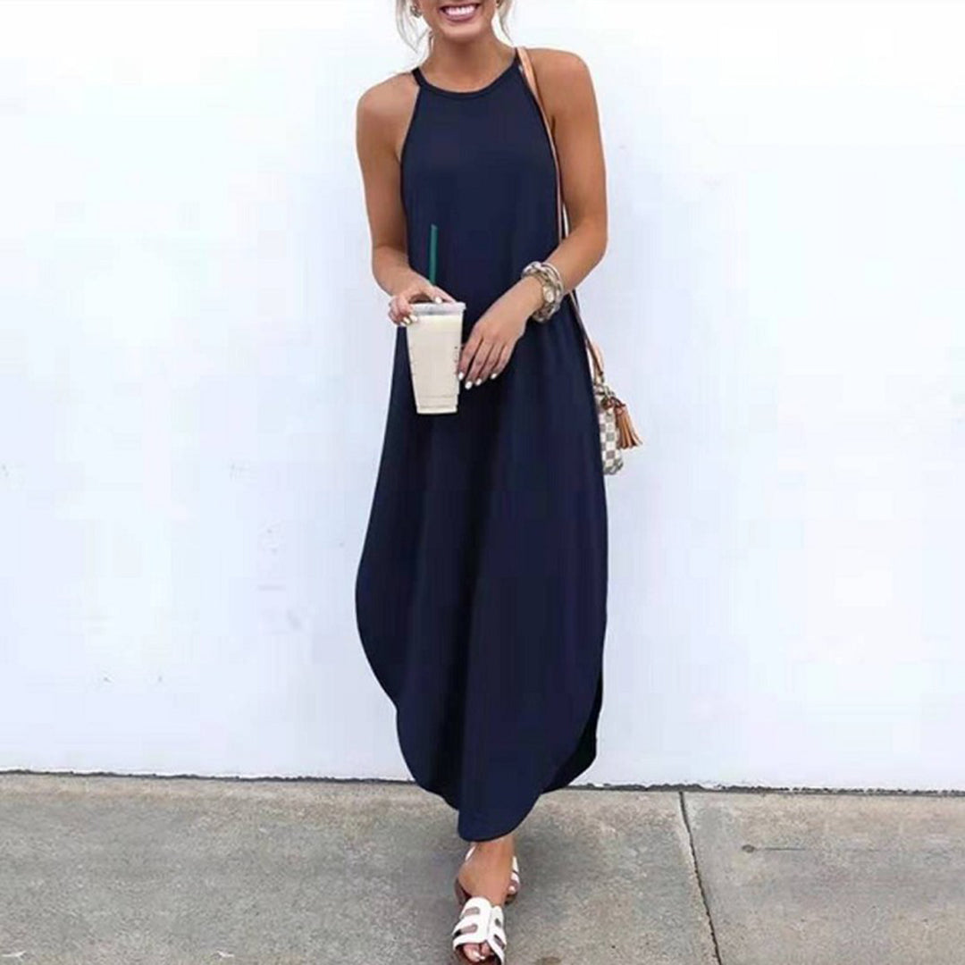 Vrouw in lange, donkerblauwe zomerjurk met halternek, houdt een ijskoffie vast. Casual mode, zomerkleding, strandstijl.
