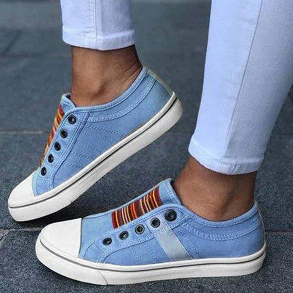 Blauwe canvas sneakers met kleurrijke strepen, zwarte veterogen en witte zolen, gedragen door persoon in witte broek. Casual schoenen, trendy stijl.