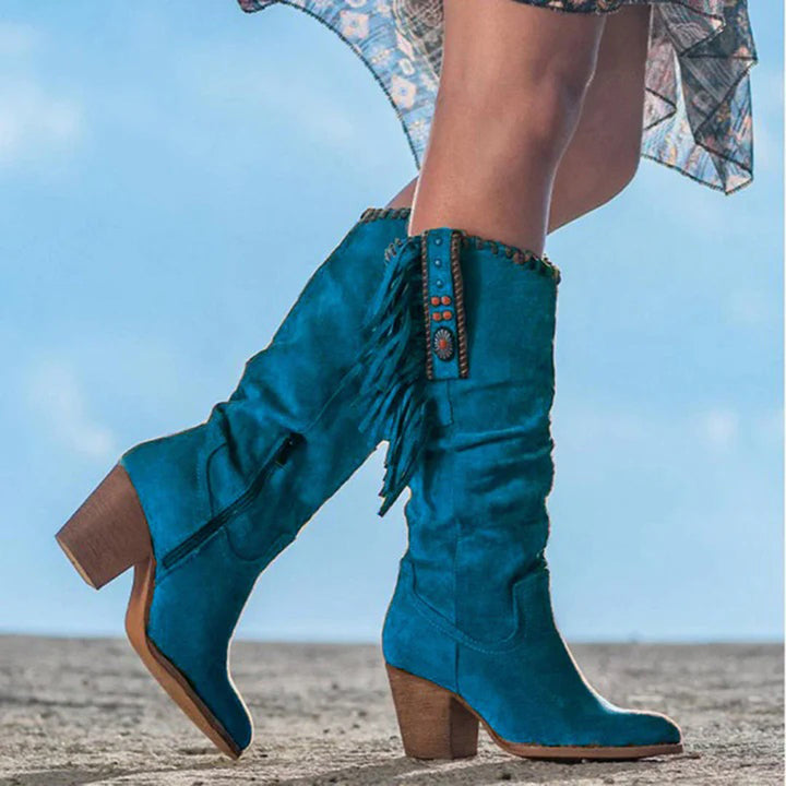 Blauwe suède cowboylaarzen met hak, franjes en decoratieve studs, gedragen door een model. Trendy dameslaarzen voor herfstmode.