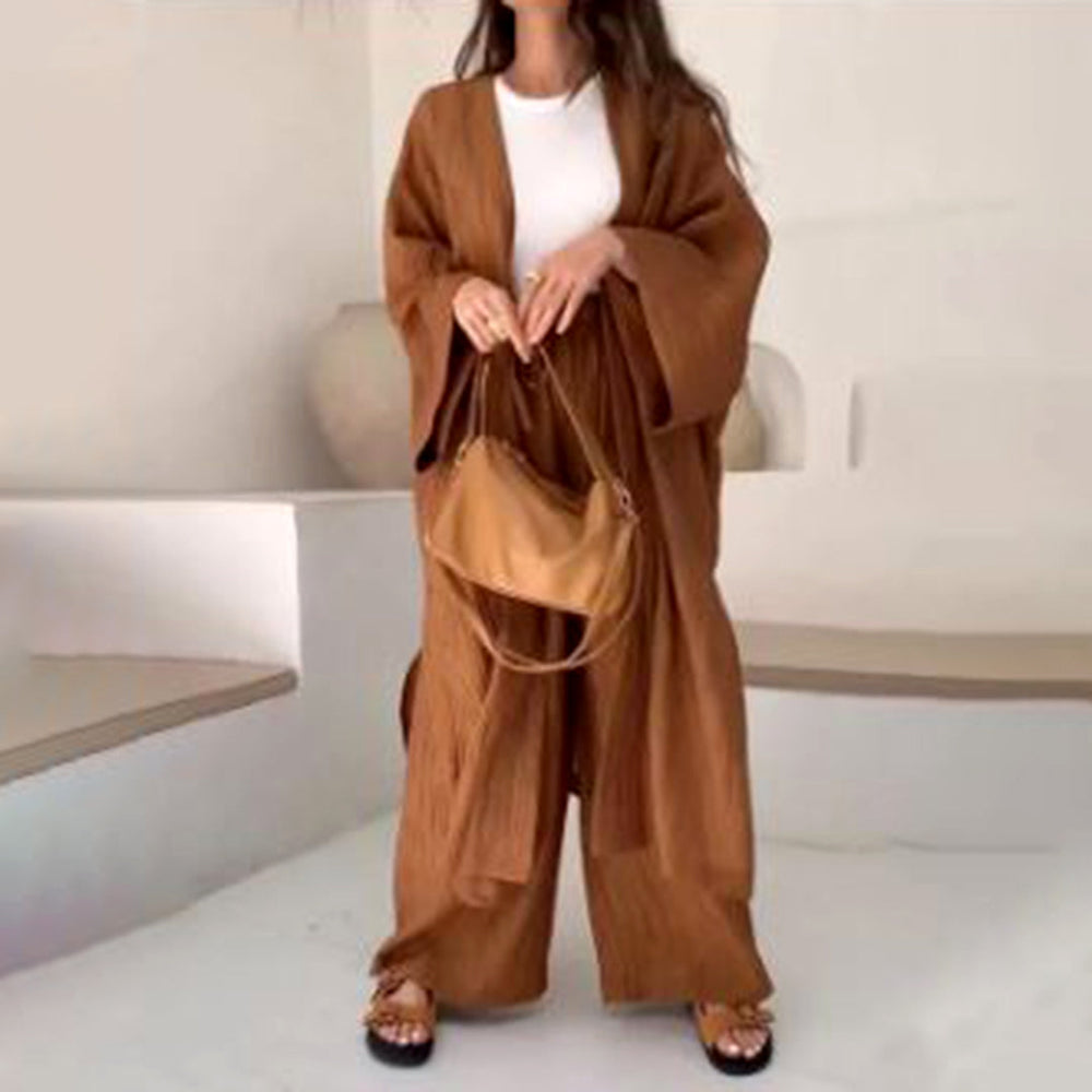 Vrouw in bruine, losse kimono en broek, witte top, met beige handtas. Modieuze dameskleding, casual stijl, comfortabele outfit.