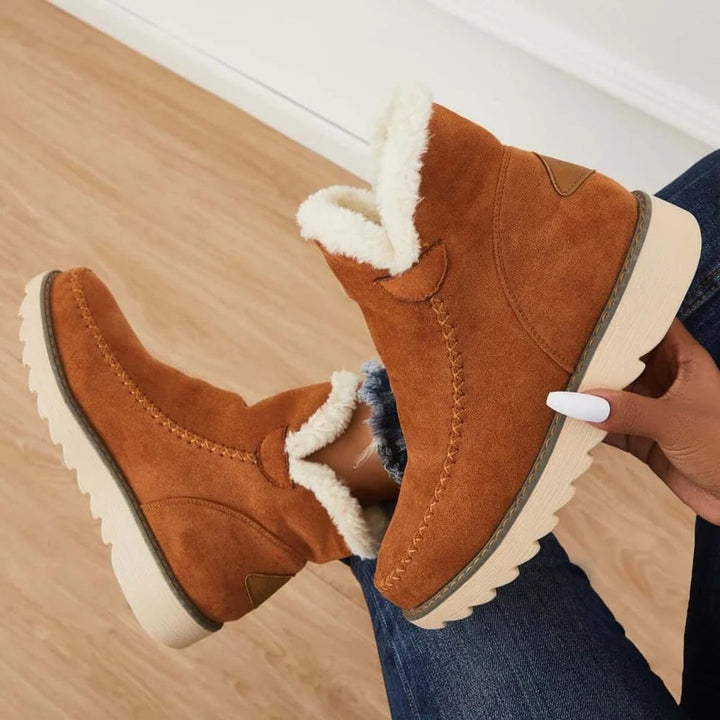Bruine suède enkellaarsjes met witte voering, comfortabele winterlaarzen voor dames, modieuze en warme schoenen op houten vloer.