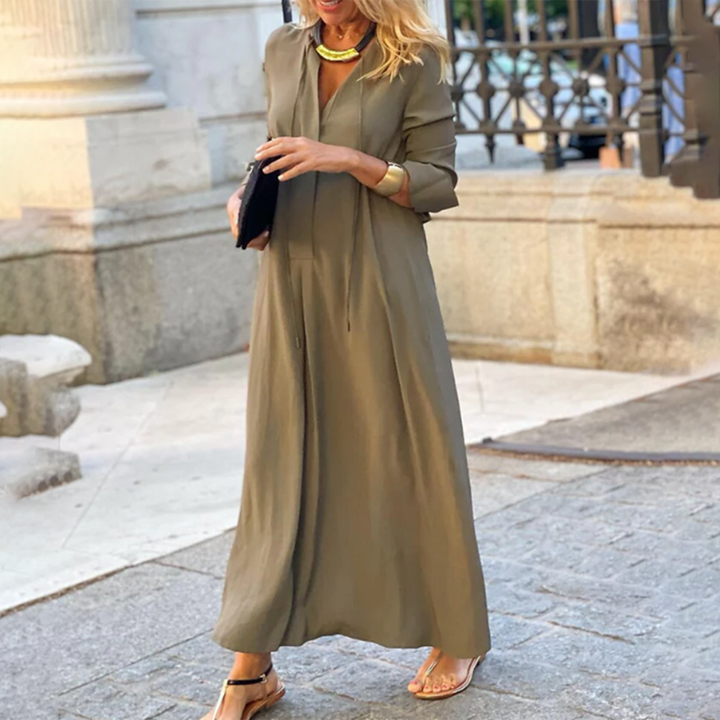 Vrouw in lange bruine jurk met gouden ketting en zwarte clutch, staand op straat. Stijlvolle zomeroutfit, casual chique mode, stedelijke achtergrond.