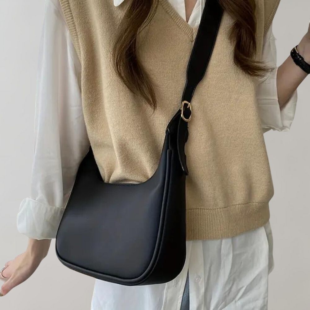 Zwarte schoudertas van PU-leer, gedragen door vrouw in beige trui en witte blouse. Stijlvolle crossbody tas voor dames, modieuze accessoire.