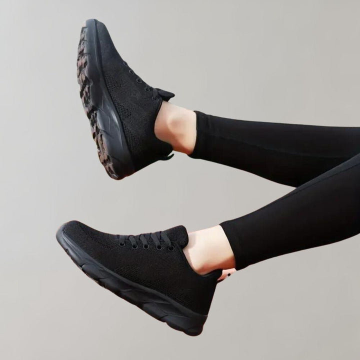 Zwarte sportschoenen met dikke zool, gedragen door persoon in zwarte legging. Comfortabele sneakers voor dagelijks gebruik en sportactiviteiten.