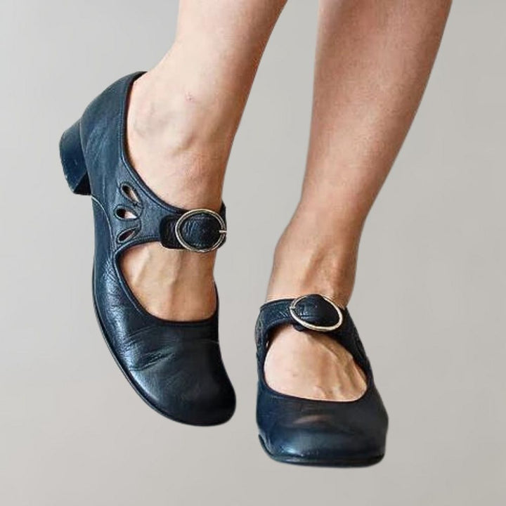 Zwarte leren Mary Jane schoenen met lage hak en decoratieve uitsnijdingen, gedragen door een persoon. Comfortabele damesmode, stijlvolle schoenen.