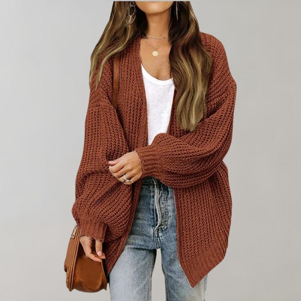 Vrouw in bruine gebreide cardigan, witte top en jeans, met bruine schoudertas. Modieuze herfstoutfit, casual dameskleding, trendy stijl.