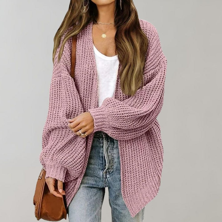 Roze gebreid damesvest, oversized pasvorm, gecombineerd met witte top en blauwe jeans. Modieuze casual outfit, perfect voor herfst en winter.