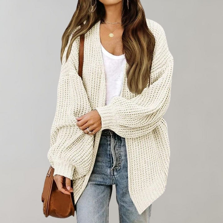 Vrouw in gebreid beige vest, witte top en jeans, met bruine schoudertas. Modieuze herfstoutfit, casual dameskleding, comfortabele stijl.