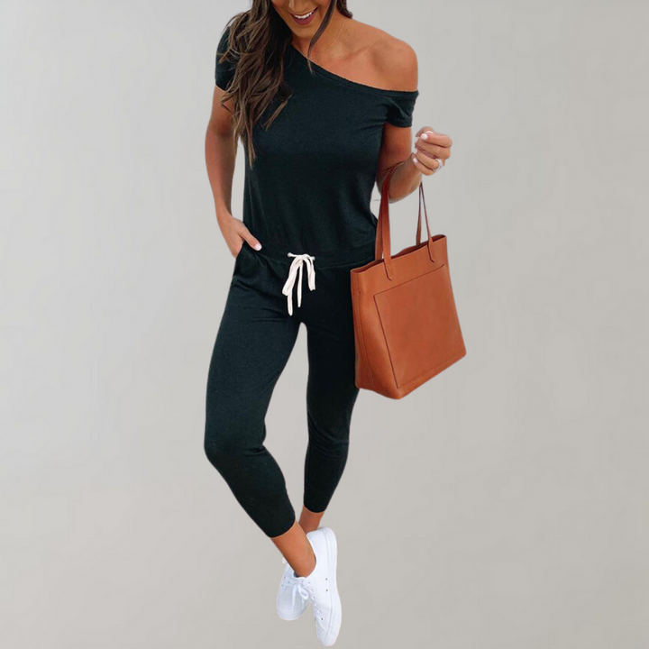 Vrouw in zwarte off-shoulder jumpsuit met witte sneakers en bruine handtas. Modieuze dameskleding, casual outfit, trendy stijl.