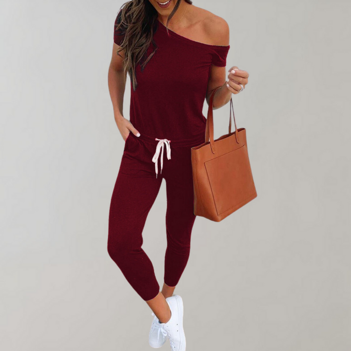 Vrouw in rode off-shoulder jumpsuit met witte sneakers en bruine handtas. Modieuze dameskleding, casual outfit, trendy stijl.