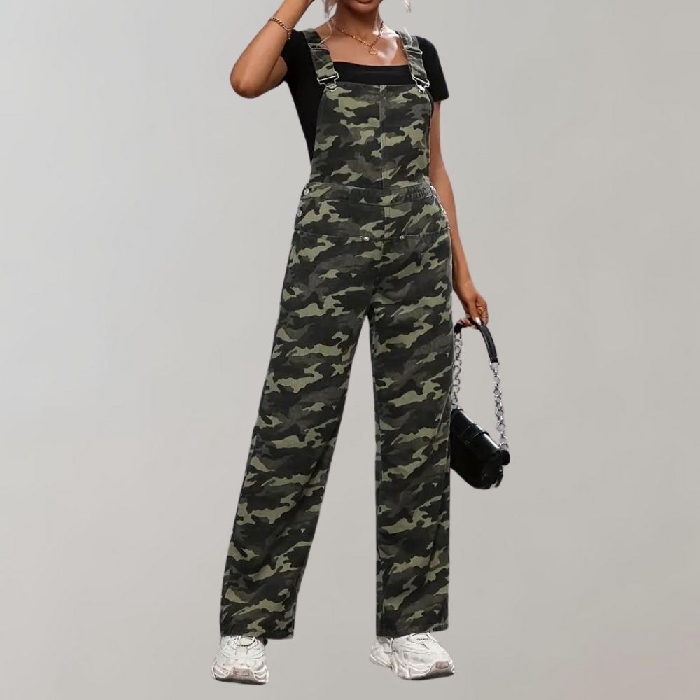 Vrouw in camouflage tuinbroek met zwarte top en witte sneakers, houdt een zwarte tas vast. Modieuze dameskleding, casual streetwear stijl.