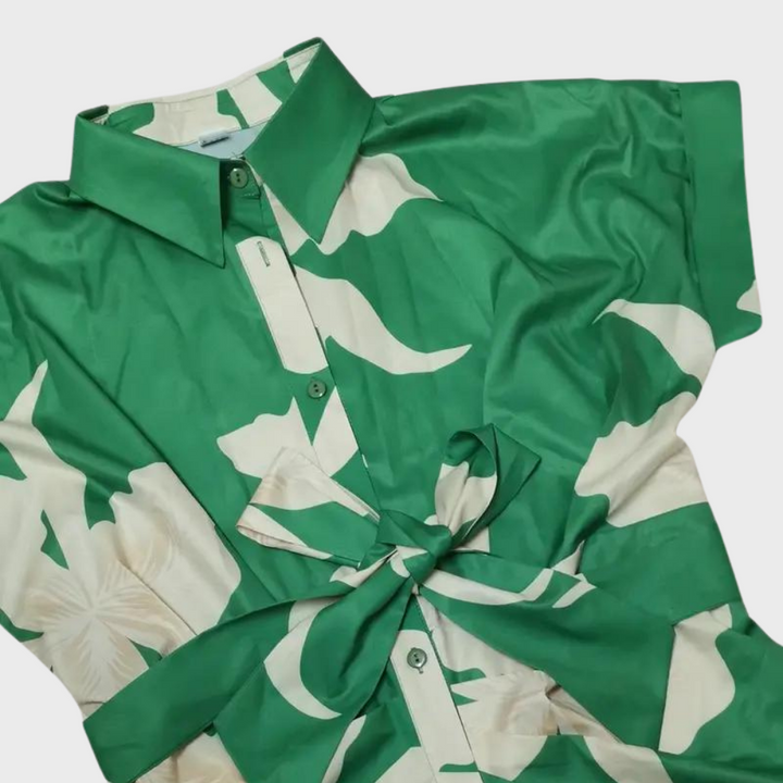 Groene damesblouse met witte bloemenprint en strikdetail, korte mouwen en kraag. Modieuze zomerblouse, ideaal voor casual en chique outfits.
