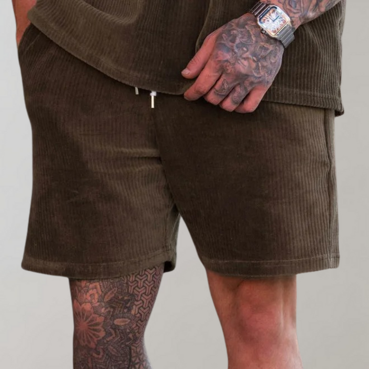 Bruine corduroy korte broek voor heren, gedragen door een getatoeëerde man. Comfortabele pasvorm, ideaal voor casual zomeroutfits.