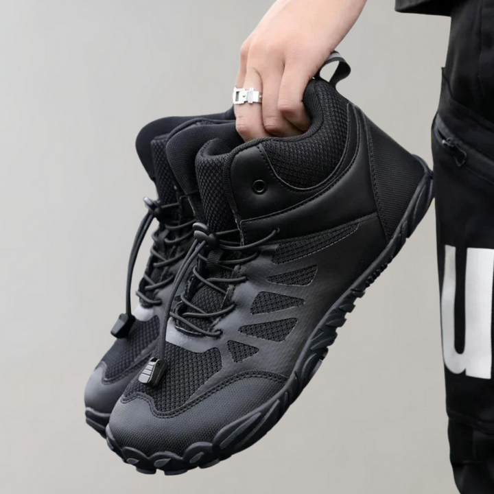 Zwarte wandelschoenen met ademend mesh en stevige zool, vastgehouden door een hand. Ideaal voor outdoor activiteiten en avontuurlijke wandelingen.