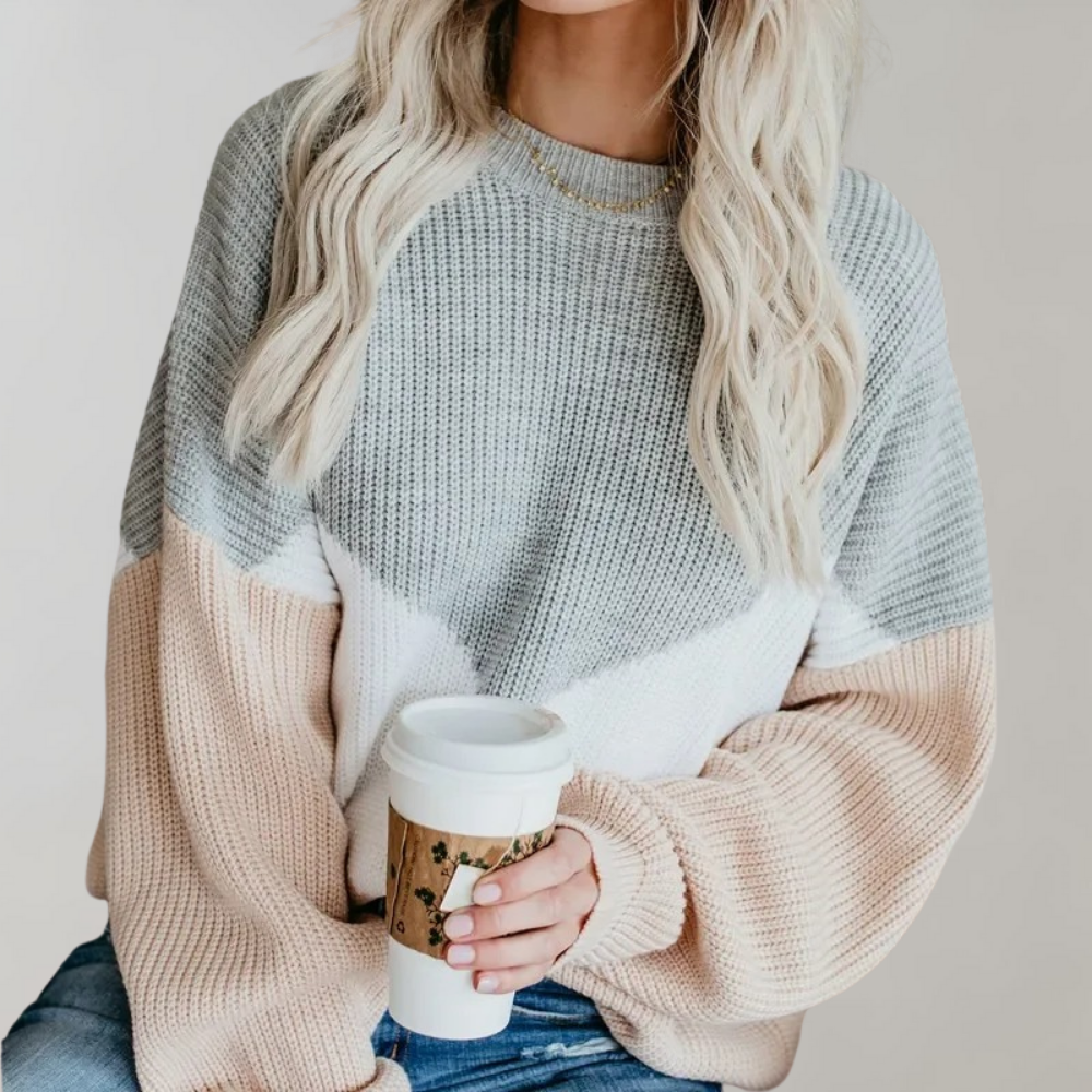 Vrouw in gebreide trui met grijs, wit en roze patroon, houdt een koffiebeker vast. Modieuze dameskleding, casual herfststijl.