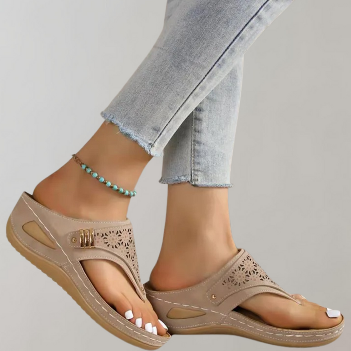 Beige dames sandalen met sleehak, open teen en geperforeerd bloemmotief, gedragen met lichtblauwe jeans. Comfortabele zomerschoenen.