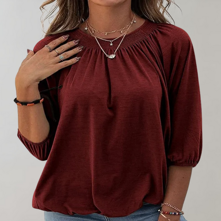 Vrouw draagt bordeauxrode blouse met driekwart mouwen, gerimpelde halslijn en sieraden. Modieuze dameskleding, casual stijl.