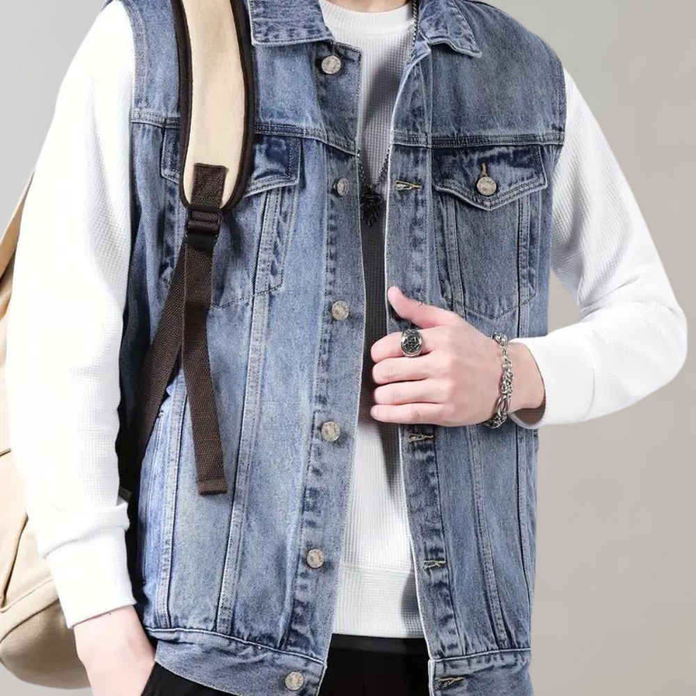 Man in spijkerjack met witte trui en rugzak. Modieuze casual outfit, denim vest, zilveren sieraden. Trendy herenkleding, streetwear stijl.