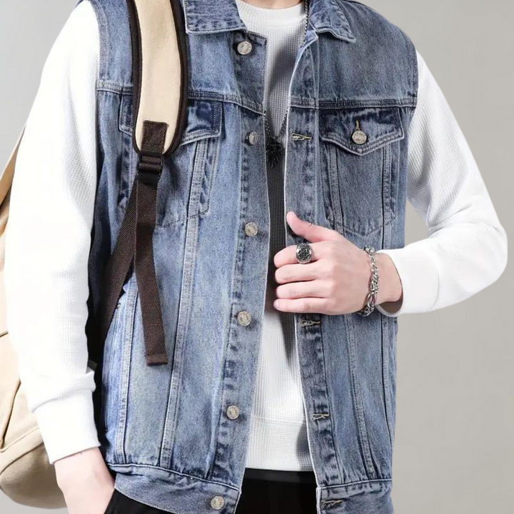 Man in spijkerjack met witte trui en rugzak. Modieuze casual outfit, denim vest, zilveren sieraden. Trendy herenkleding, streetwear stijl.