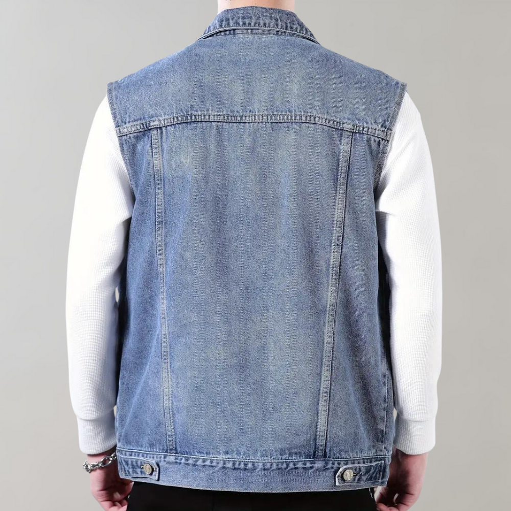 Achteraanzicht van een man in een blauwe spijkerjas zonder mouwen, gedragen over een witte trui. Modieuze denim look, casual herenkleding.