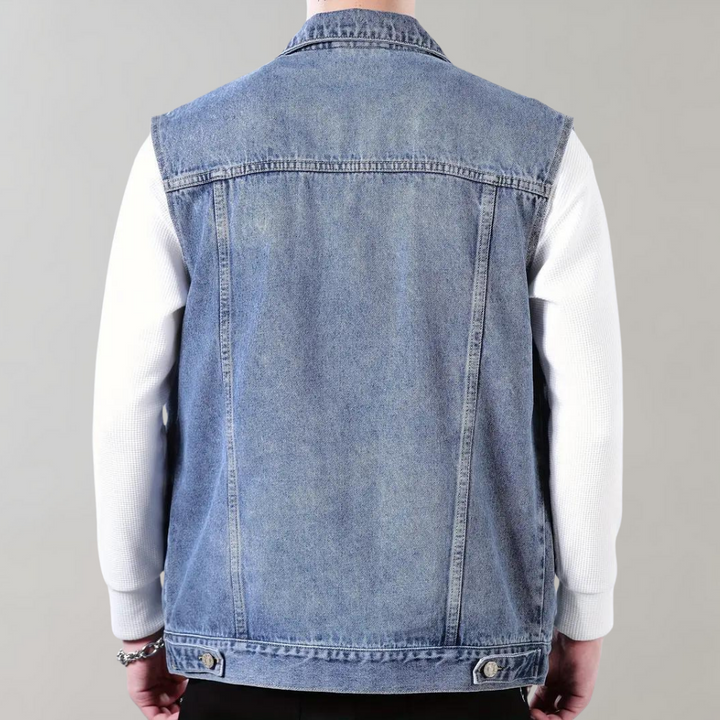 Achteraanzicht van een man in een blauwe spijkerjas zonder mouwen, gedragen over een witte trui. Modieuze denim look, casual herenkleding.