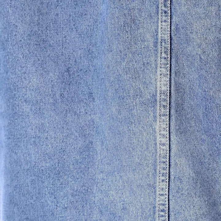 Lichtblauwe denimstof close-up met zichtbare textuur en stiknaad, ideaal voor modeontwerp, jeans en kledingproductie.