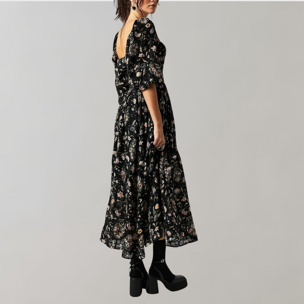 Zwarte bloemenjurk met korte mouwen en open rug, gedragen door model. Elegante damesmode, perfect voor avondkleding. Trendy en stijlvol ontwerp.