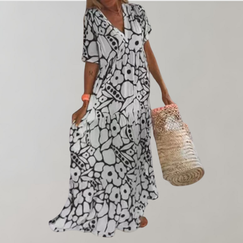 Zwart-witte bloemenjurk met korte mouwen, gedragen door vrouw met rieten tas. Zomerse boho-stijl, casual en elegant. Perfect voor stranddagen.