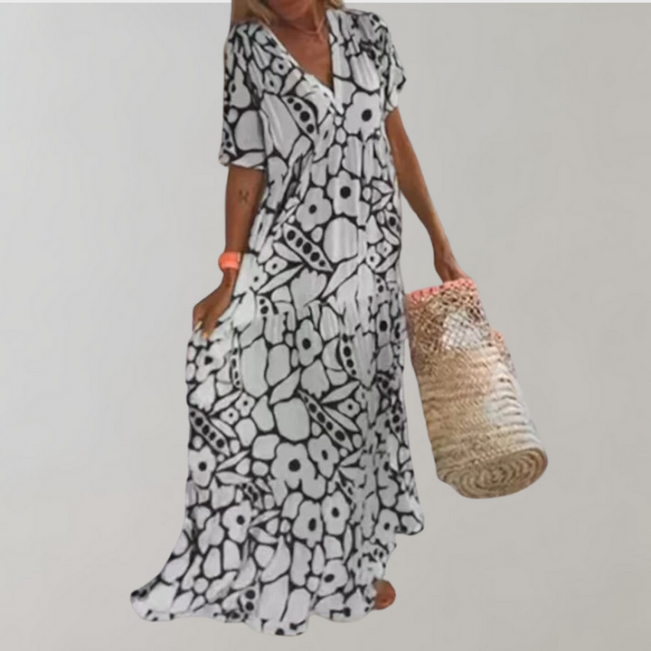 Zwart-witte bloemenjurk met korte mouwen, gedragen door vrouw met rieten tas. Zomerse boho-stijl, casual en elegant. Perfect voor stranddagen.