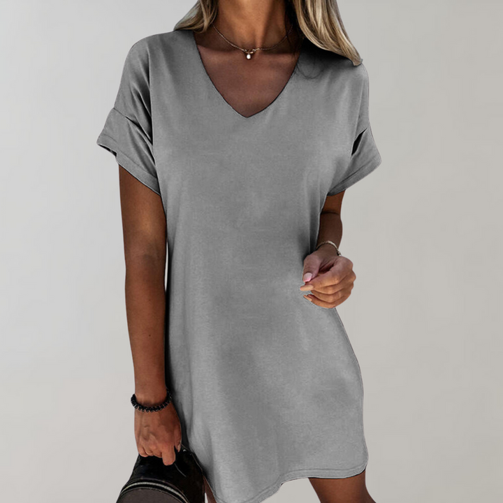 Grijze damesjurk met V-hals en opgerolde mouwen, gedragen door model. Perfect voor casual en zomerse looks. Comfortabele en stijlvolle pasvorm.