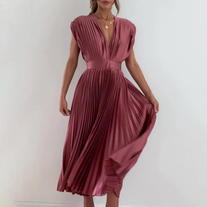 Vrouw in elegante, roze geplooide jurk met diepe V-hals, staand tegen een witte achtergrond. Perfect voor avondkleding of formele evenementen.