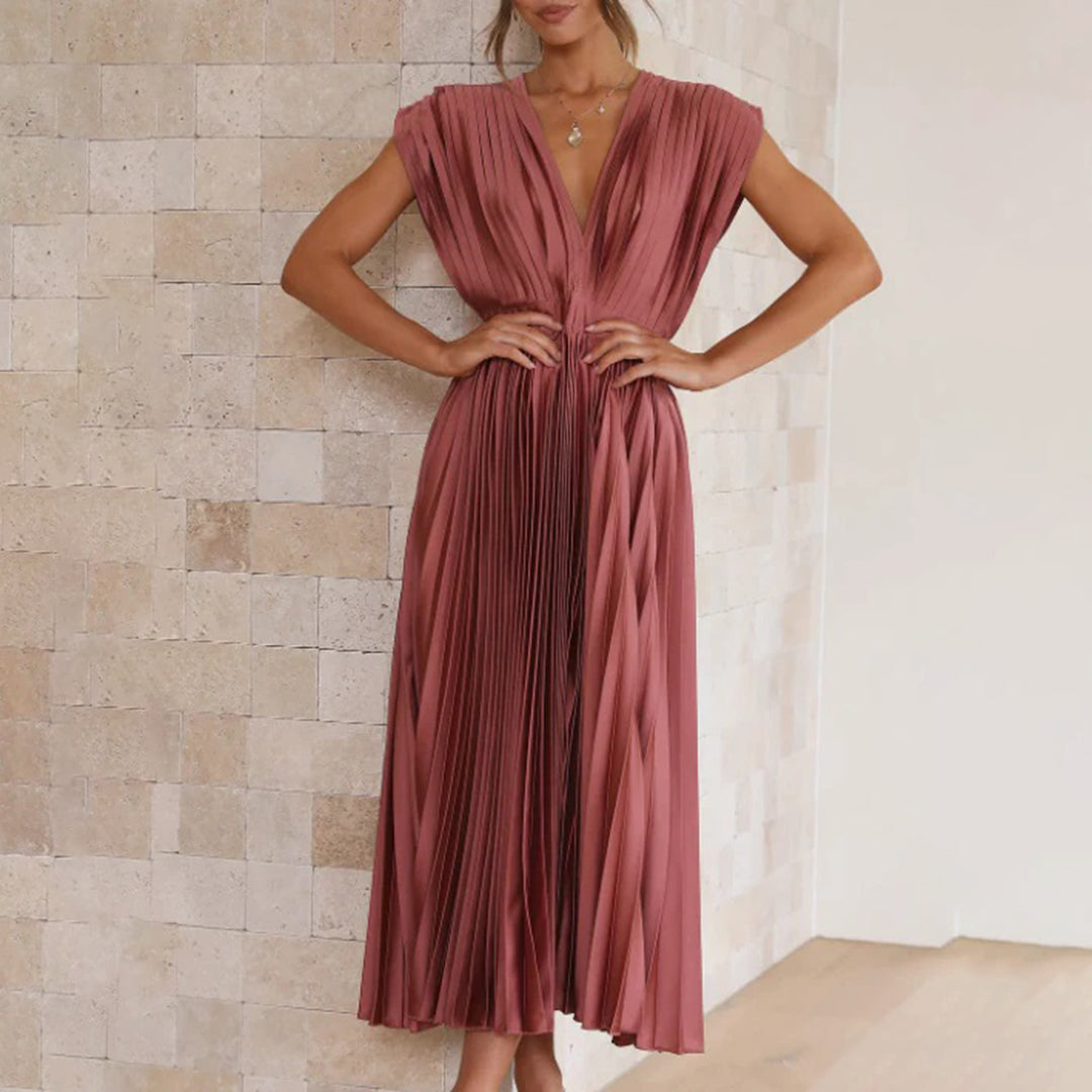 Vrouw in elegante roze geplooide jurk, staand tegen een stenen muur. Perfect voor avondkleding, modetrends, stijlvolle damesmode.
