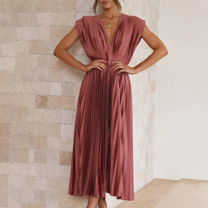 Vrouw in elegante roze geplooide jurk, staand tegen een stenen muur. Perfect voor avondkleding, modetrends, stijlvolle damesmode.