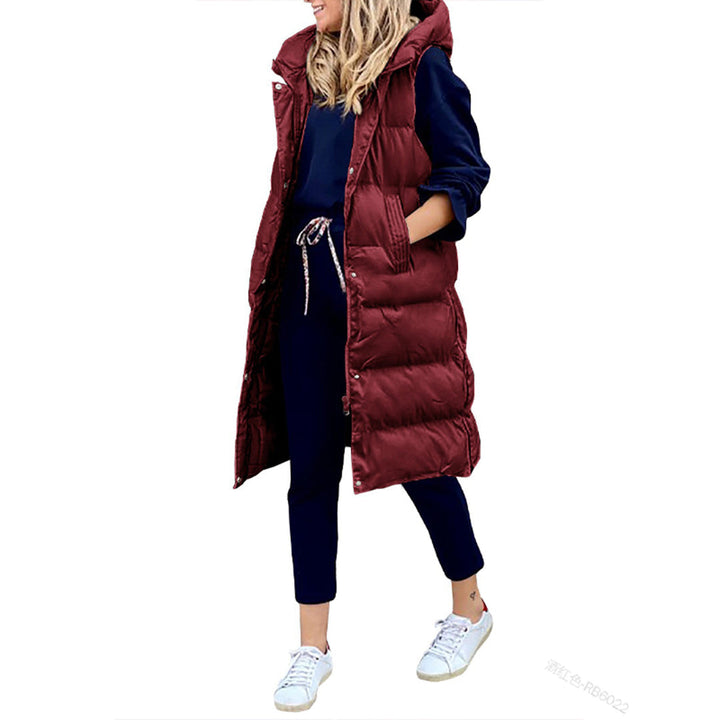 Vrouw in lange bordeauxrode gewatteerde bodywarmer, donkerblauwe trui en broek, witte sneakers. Modieuze winteroutfit voor dames.