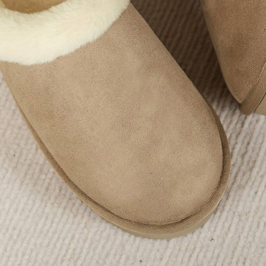 Beige suède pantoffels met witte bontvoering op een crèmekleurig tapijt. Comfortabele winterse huisschoenen voor dames.