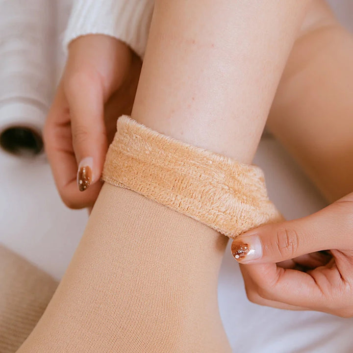 Vrouw trekt warme, beige fleece sokken aan; comfortabele winterkleding, zachte thermosokken voor koude dagen, modieuze nagels.