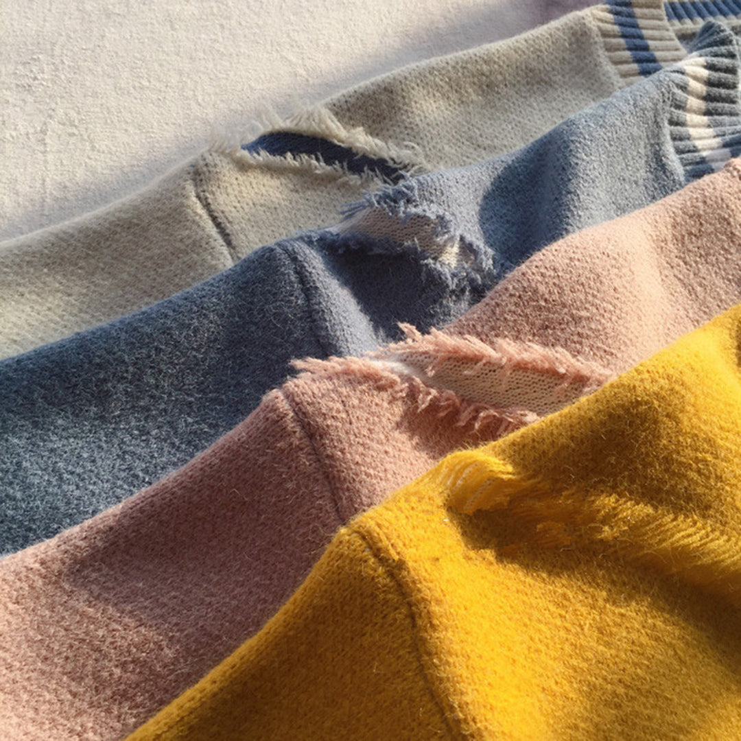 Vier kleurrijke, gerafelde truien in geel, roze, blauw en beige op een witte achtergrond. Zachte stoffen, casual mode, herfstkleding.