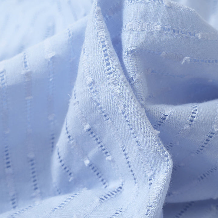 Lichtblauwe katoenen stof met opengewerkte strepen, close-up. Perfect voor zomerkleding en naaiprojecten. Zachte textuur, ademend materiaal.