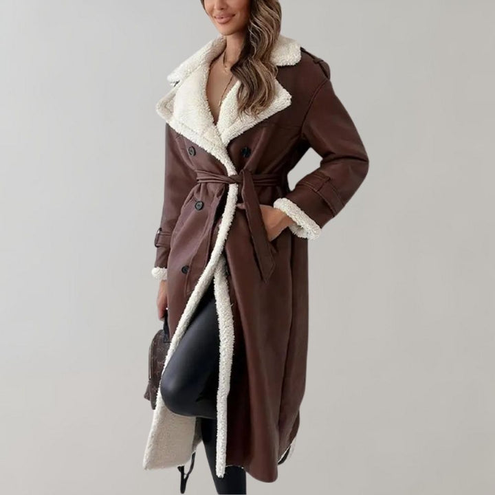 Lange bruine dames winterjas met witte fleece voering, dubbele rij knopen en ceintuur. Stijlvolle warme jas voor koude seizoenen.