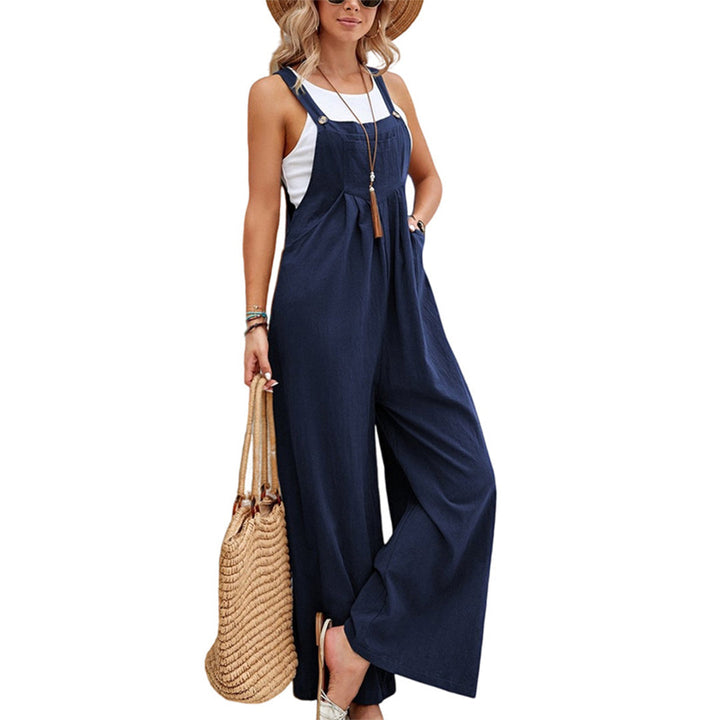 Vrouw in donkerblauwe jumpsuit met witte top, strohoed en rieten tas. Modieuze zomeroutfit, casual dameskleding, trendy accessoires.