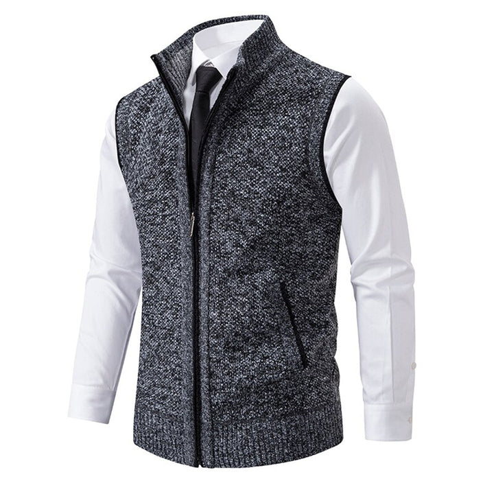 Donkergrijs herenvest met ritssluiting, gedragen over een witte overhemd en zwarte stropdas. Stijlvolle, casual herenkleding.