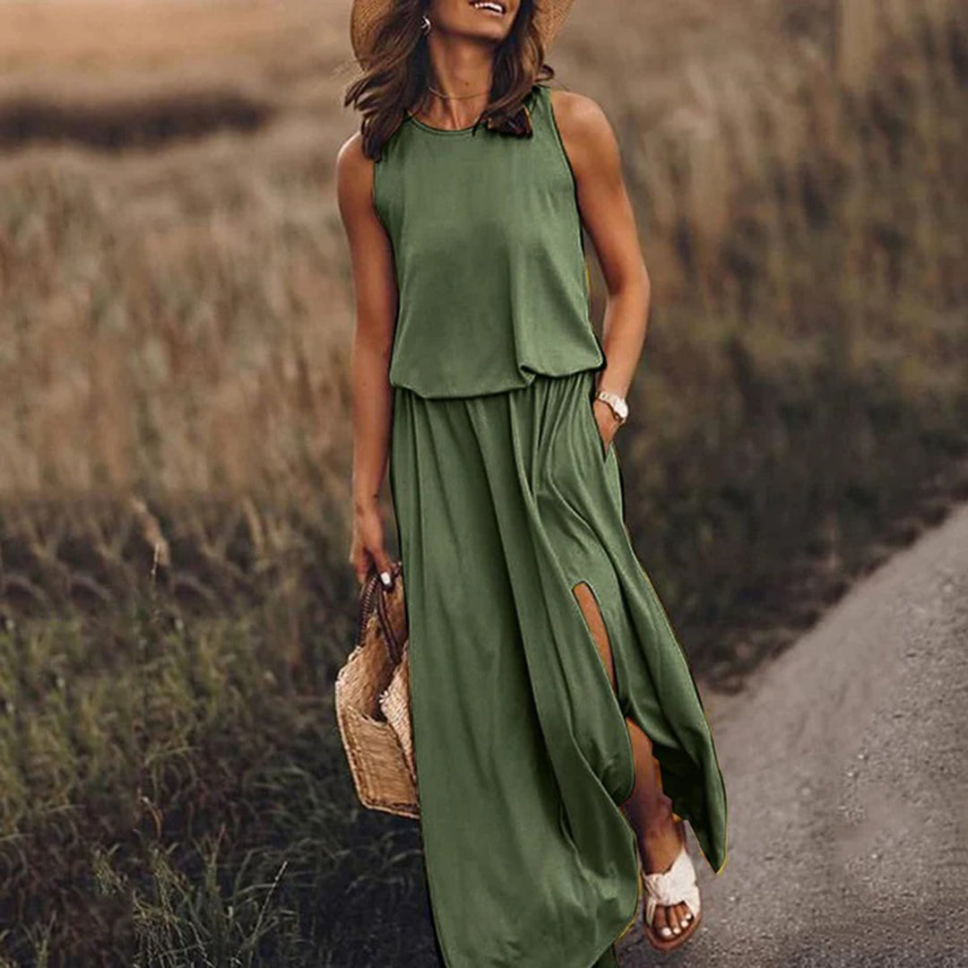 Vrouw in groene maxi-jurk met hoge split, draagt strohoed en rieten tas, wandelend op landweg. Zomermode, casual elegantie, boho-stijl.