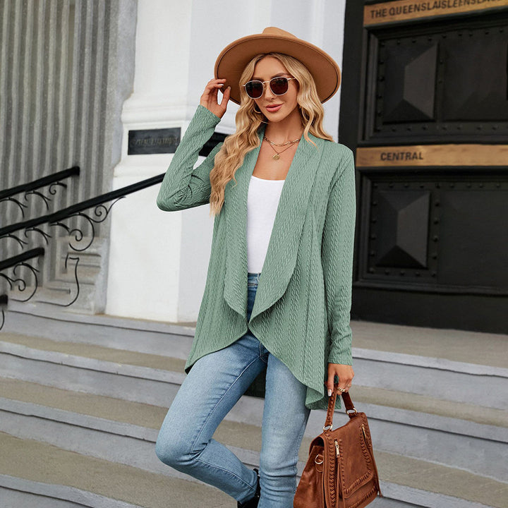 Vrouw in groene cardigan, witte top en jeans, draagt hoed en zonnebril, met bruine handtas. Stijlvolle herfstmode op trap voor historisch gebouw.