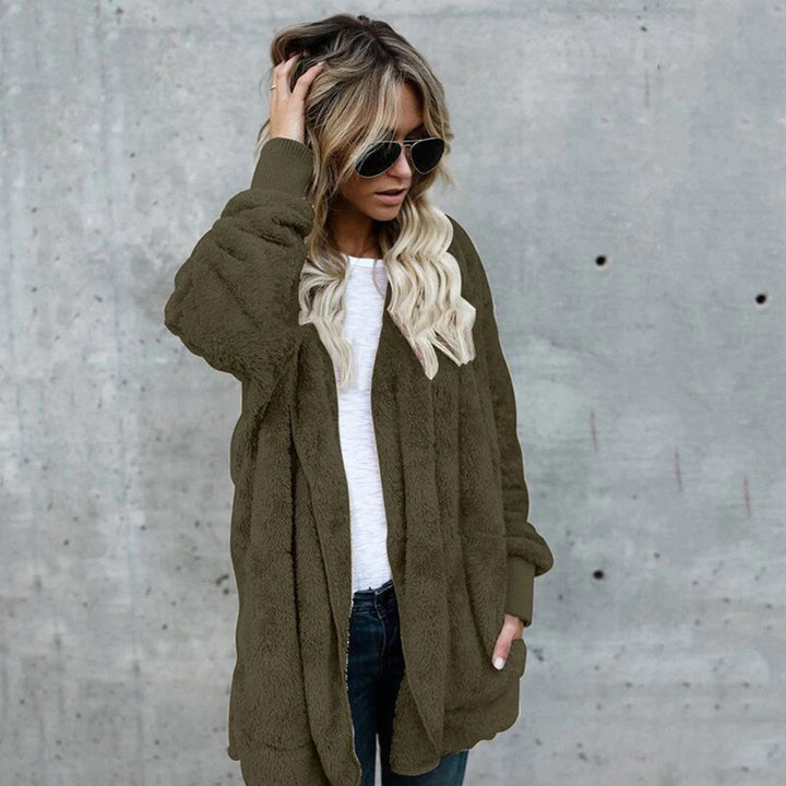 Vrouw in groene teddyjas, witte top en zonnebril tegen betonnen muur. Modieuze winterkleding, casual stijl, trendy damesmode.